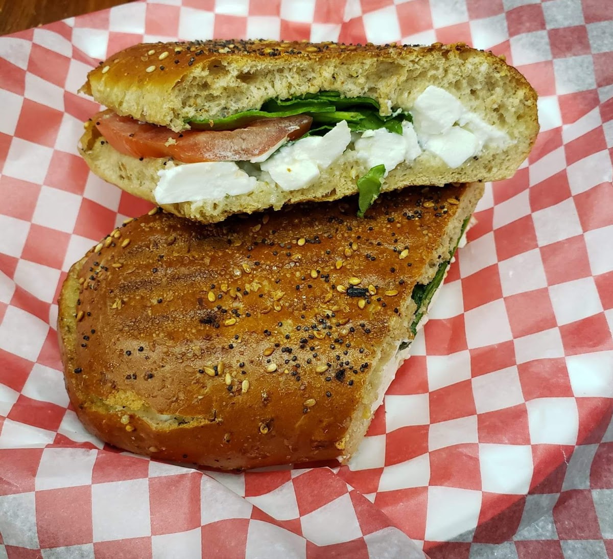 A fresh panini with feta cheese, tomato, and spinach on seeded bread in checkered paper