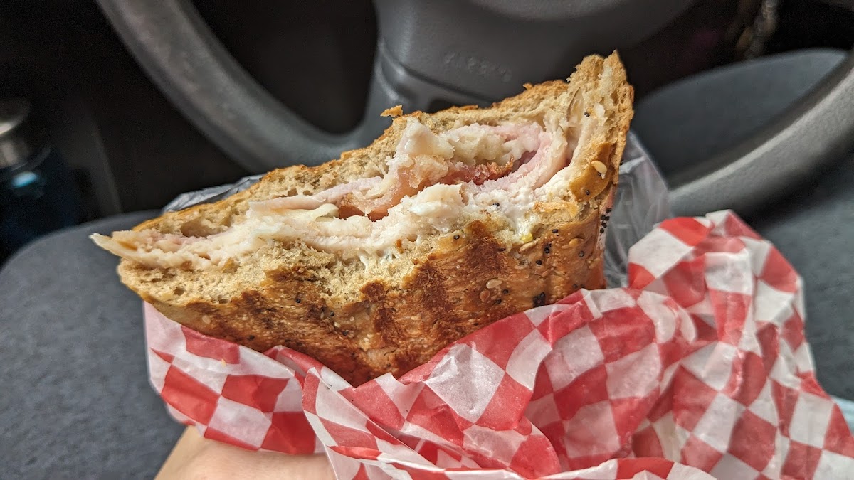 A hearty panini sandwich held up showing layers of meat and melted cheese on checkered paper