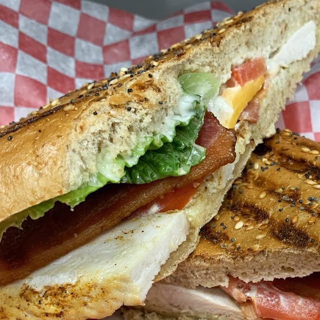 A grilled club sandwich with bacon, lettuce, tomato, and cheese on toasted bread
