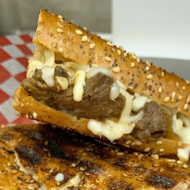 A Chuck's steak panini cut open showing tender beef and melted cheese on seeded bread