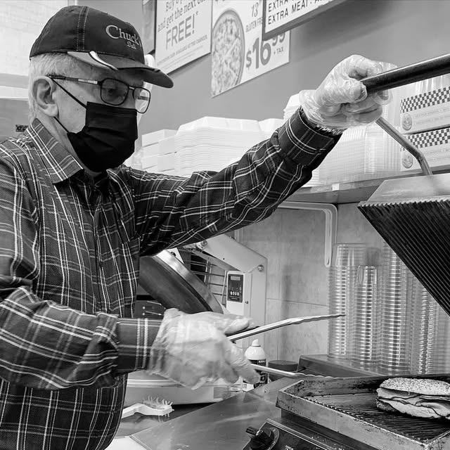 Chuck, the owner, working behind the counter at Chuck's Deli, pressing a fresh panini on the grill