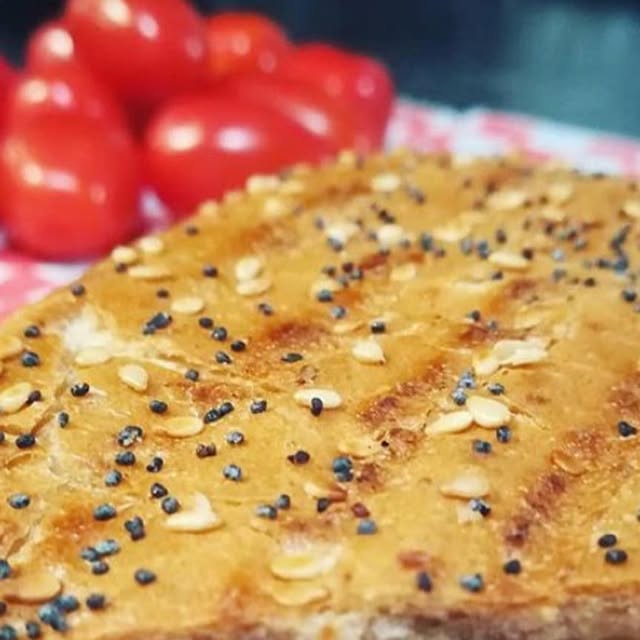 Close-up of golden toasted panini bread with sesame and poppy seeds alongside fresh tomatoes